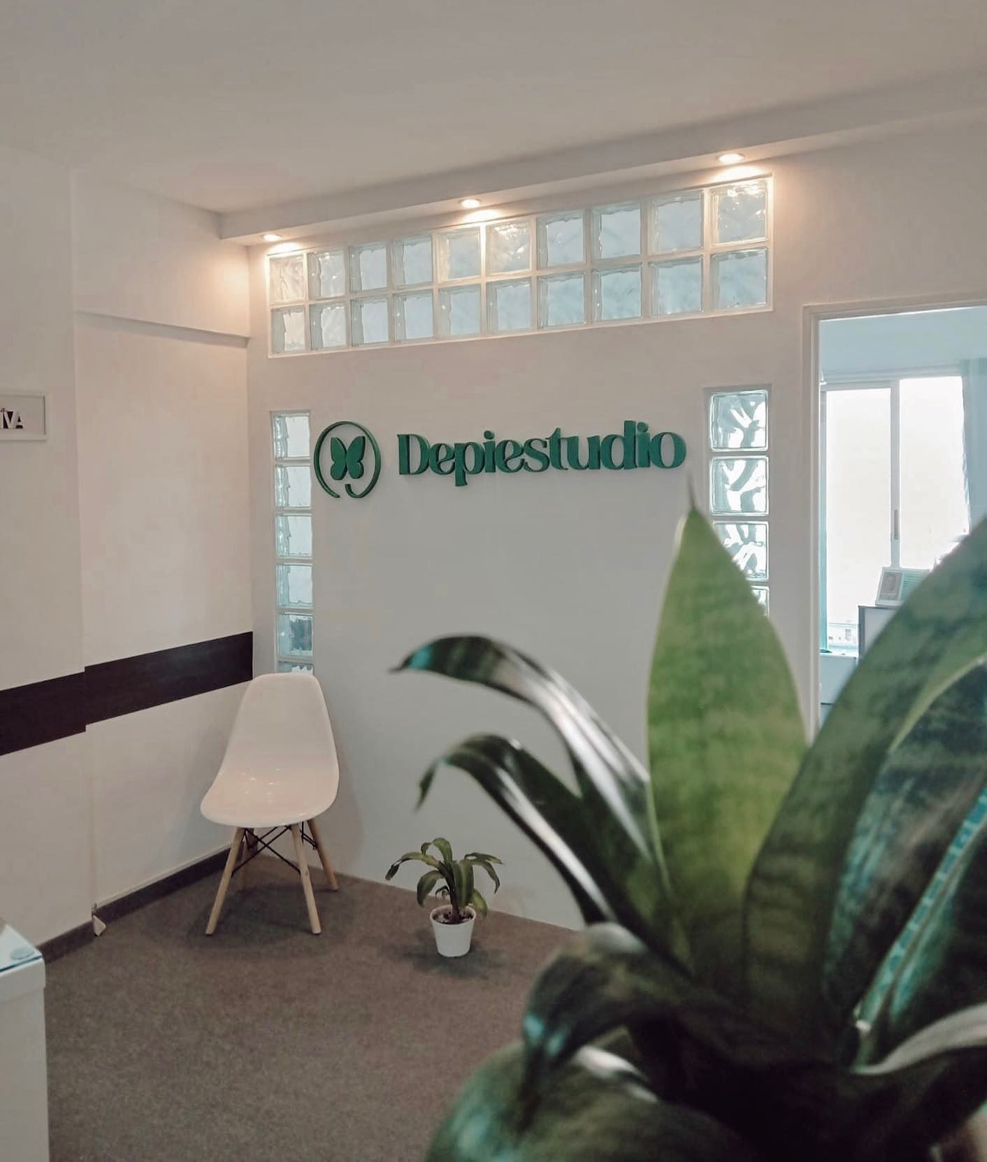 El cartel verde de Depiestudio en la recepción, entre ladrillos de vidrio, con una silla blanca y una planta